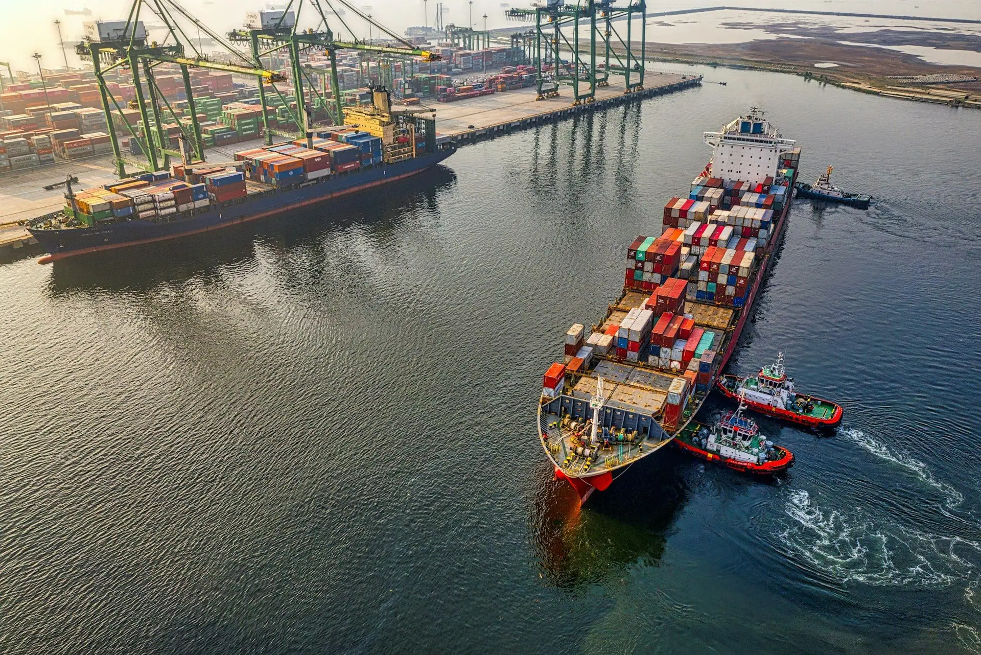 Loaded container ship guided by tugs out of a commercial port