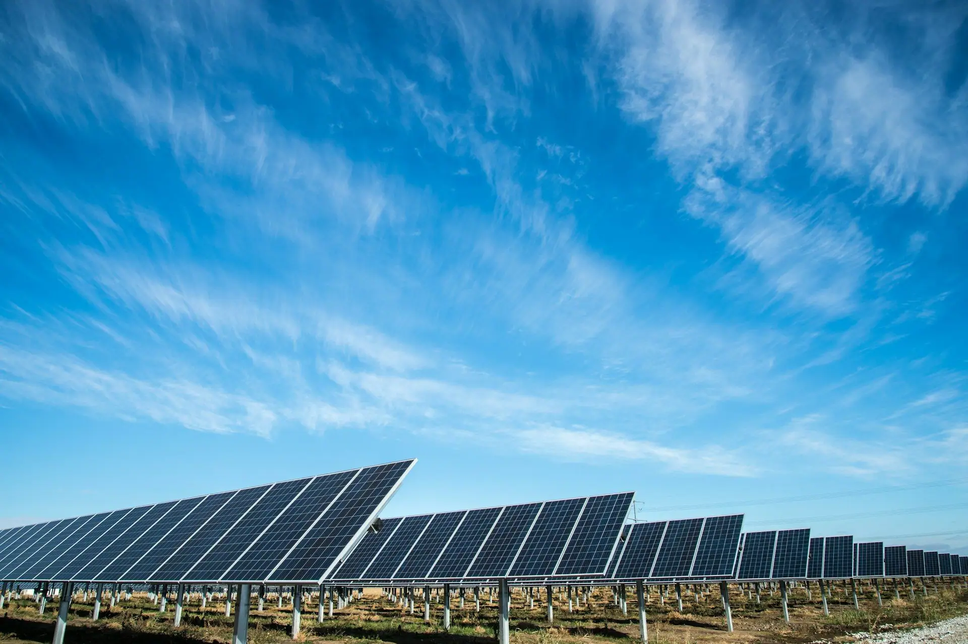 Rows of solar panels beneath a wide blue sky with high cloud